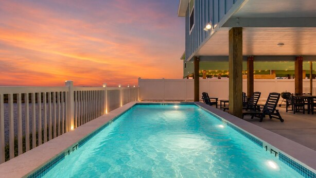 A rectangular pool with clear blue water, surrounded by a white fence, and a deck area with chairs and tables. - PP189, Private Pool, Pet Friendly, Beautiful Sunsets (Port Aransas)