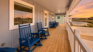 A covered porch with wooden flooring and blue chairs, overlooking a body of water and a distant landscape. - PP189, Private Pool, Pet Friendly, Beautiful Sunsets (Port Aransas)