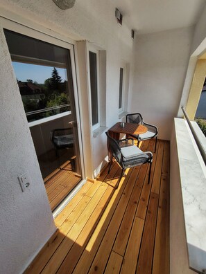 Ein Balkon mit Holzboden, einem Tisch und Stühlen sowie einer Schiebeglastür.