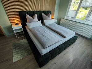 Ein modernes Schlafzimmer mit Bett, Nachttischen, Heizkörper und einem Fenster mit Ausblick.