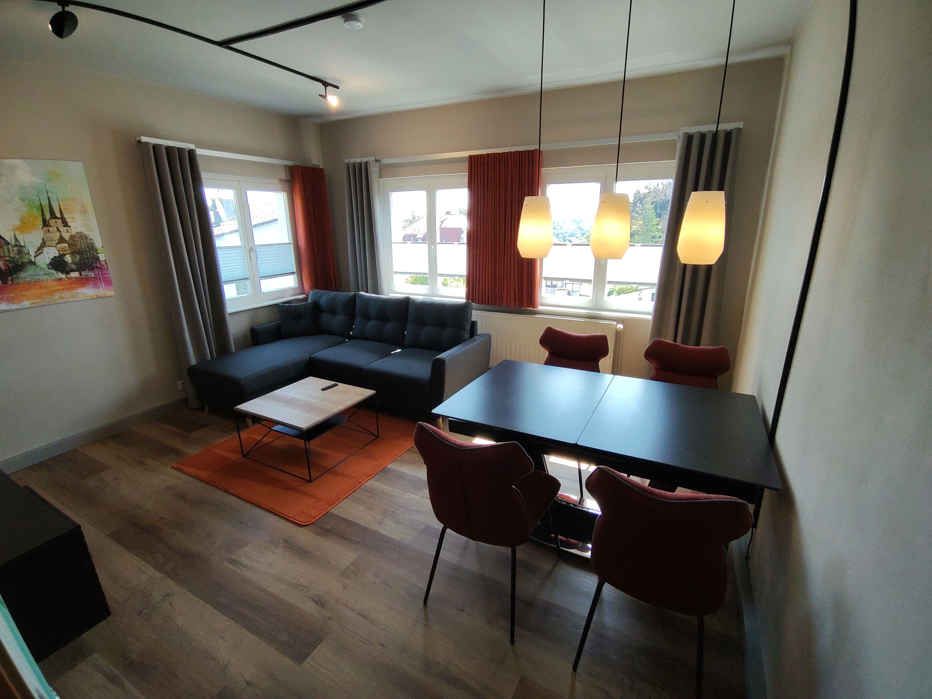 En moderne stue med en hjørnesofa, et spisebord med stole og store vinduer med gardiner.