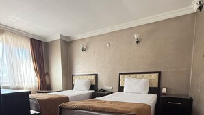 Une chambre d’hôtel avec deux lits, un bureau, une chaise, une fenêtre avec des rideaux et un luminaire fixé au mur.