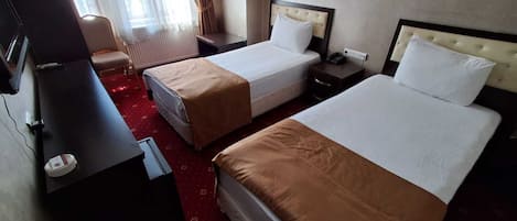 Une chambre d’hôtel avec deux lits, un bureau, une chaise, une télévision et une fenêtre avec des rideaux.