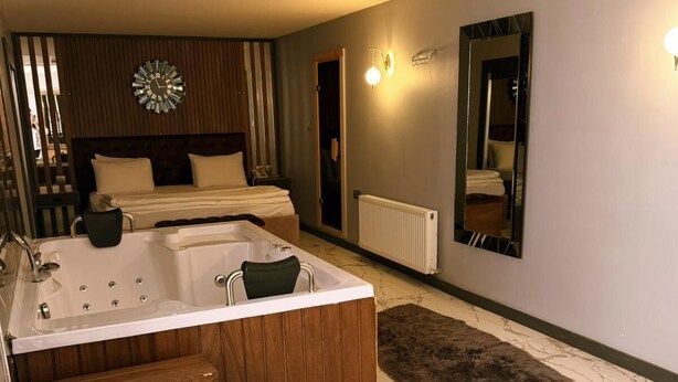 Une chambre d’hôtel moderne avec un grand lit, une salle de bain séparée avec une baignoire, un miroir et une horloge au mur.