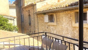 Ein Balkon mit Tisch und Stühlen, im Hintergrund steinerne Gebäude und ein klarer Himmel.