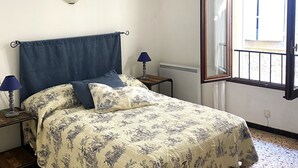 Ein Schlafzimmer mit einem Bett, zwei Nachttischlampen, einem Fenster mit geöffnetem Vorhang und einer Heizung.