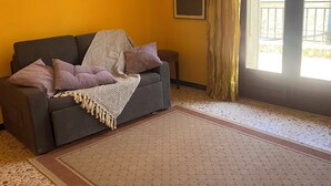 Ein Wohnzimmer mit einer Couch, einem gemusterten Teppich und einer Schiebetür zu einem Außenbereich.