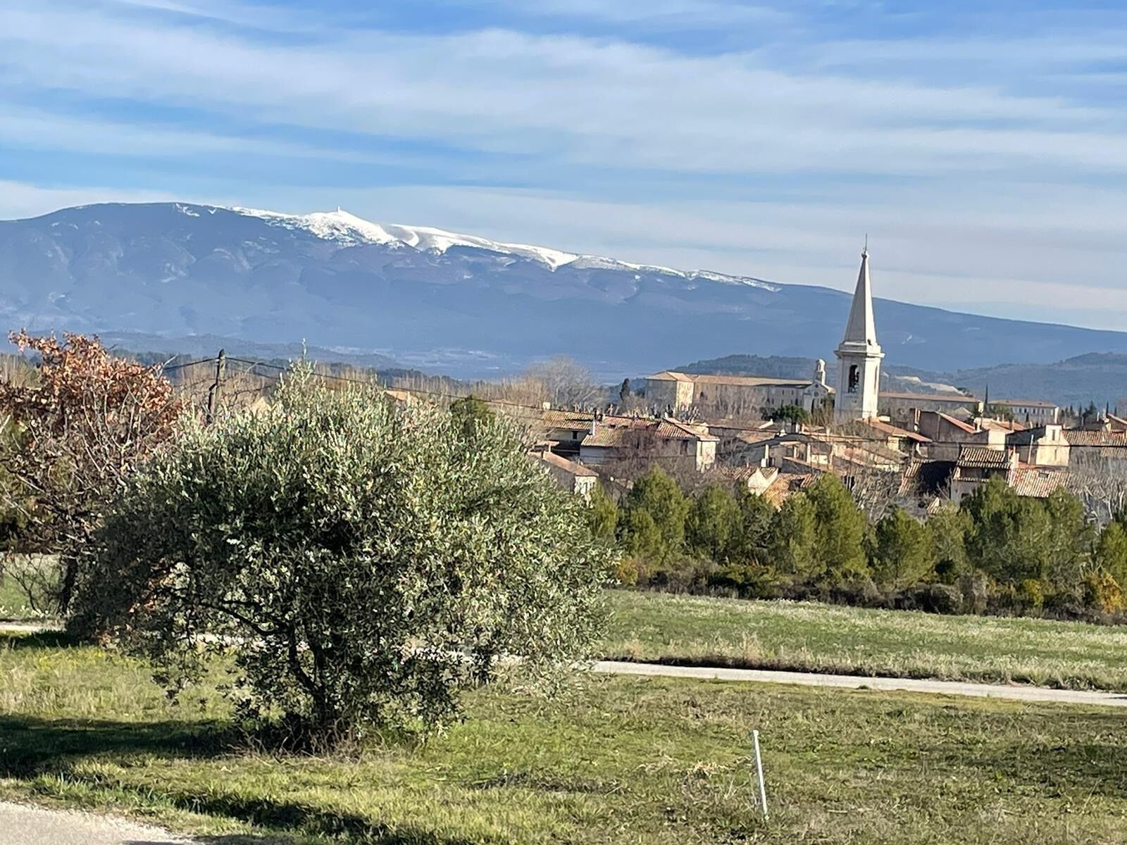 Une ville dont l’église se distingue par son flèche imposante, avec une montagne enneigée en arrière-plan et un ciel dégagé.