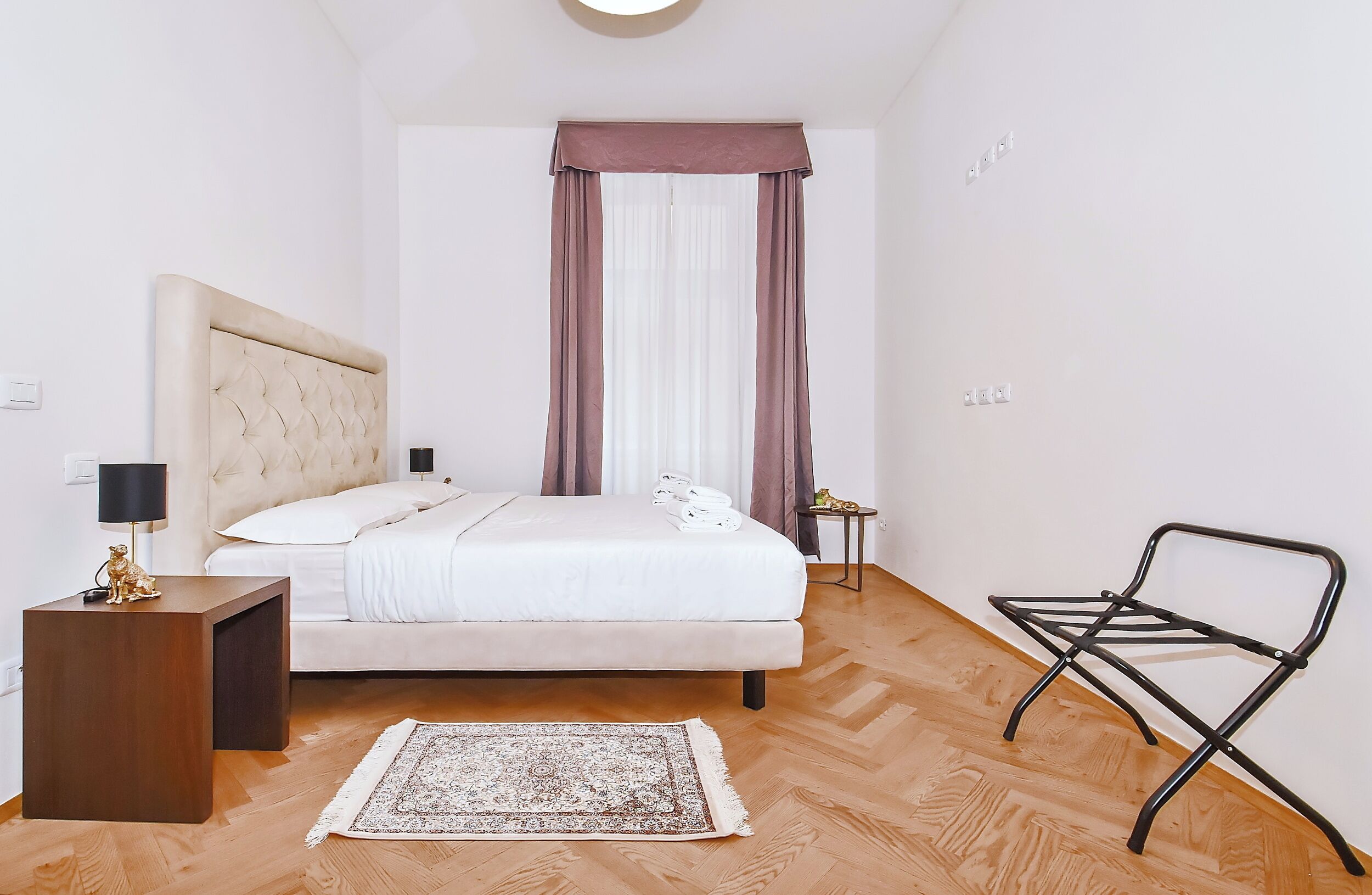 A bedroom with a bed, bedside table, lamp, rug, and a chair.