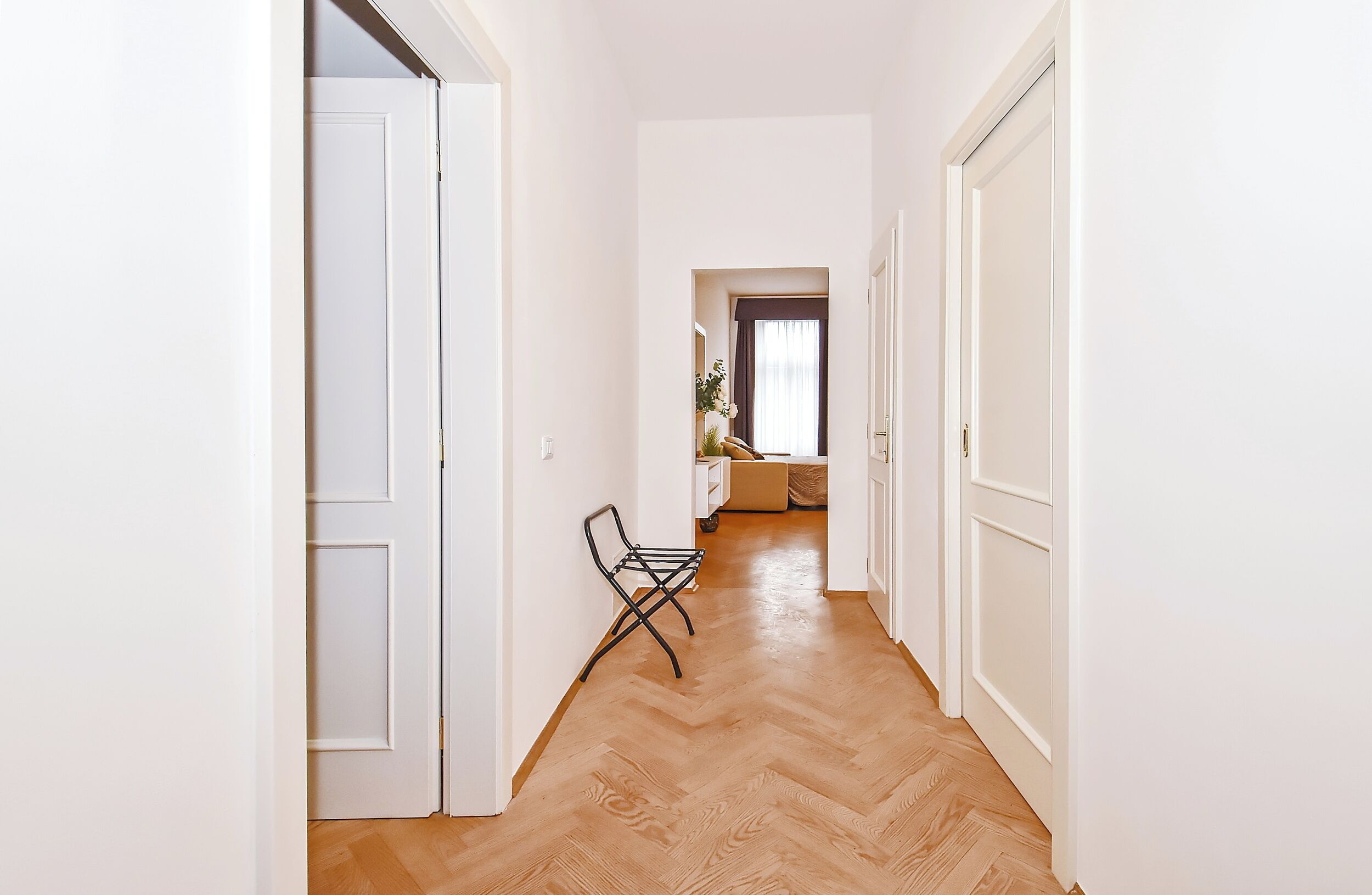 A hallway with white walls, wooden flooring, and a chair.