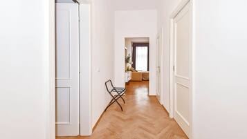 A hallway with white walls, wooden flooring, and a chair.