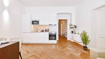 A modern kitchen with white cabinetry, a built-in oven, and a herringbone wood floor.