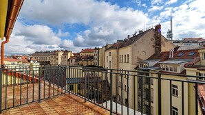 Ein Balkon mit Fliesenboden, Metallgeländer und Blick auf benachbarte Gebäude sowie einen Turm.