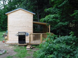 A wooden cabin with a deck, surrounded by dense forest.