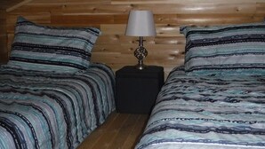 A small, cozy room with two beds, a nightstand, and a lamp. - Rustic Bunkie with Lake Front View! (Echo Bay)