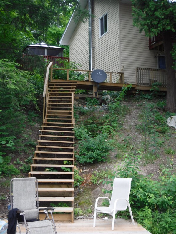 A wooden staircase leading up to a house with a satellite dish, surrounded by greenery.