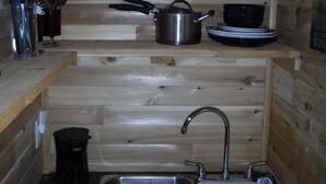 A compact kitchen with wooden walls, a sink, a pot, and various utensils. - Rustic Bunkie with Lake Front View! (Echo Bay)