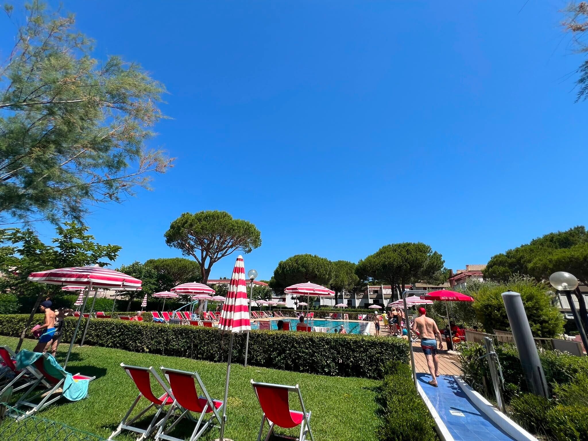 Un espace piscine agrémenté de parasols à rayures rouges et blanches, de chaises longues et d’un ciel d’un bleu limpide.