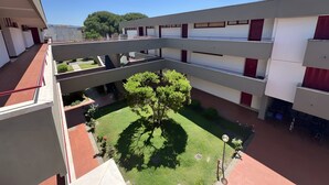 Un edifici de diverses plantes amb balcons, un pati central amb un arbre i un cel blau clar.