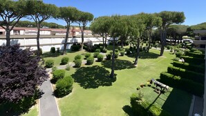 Un jardí ben cuidat amb arbustos i arbres perfectament tallejats, un camí pavimentat i un edifici amb teulada vermella al fons.