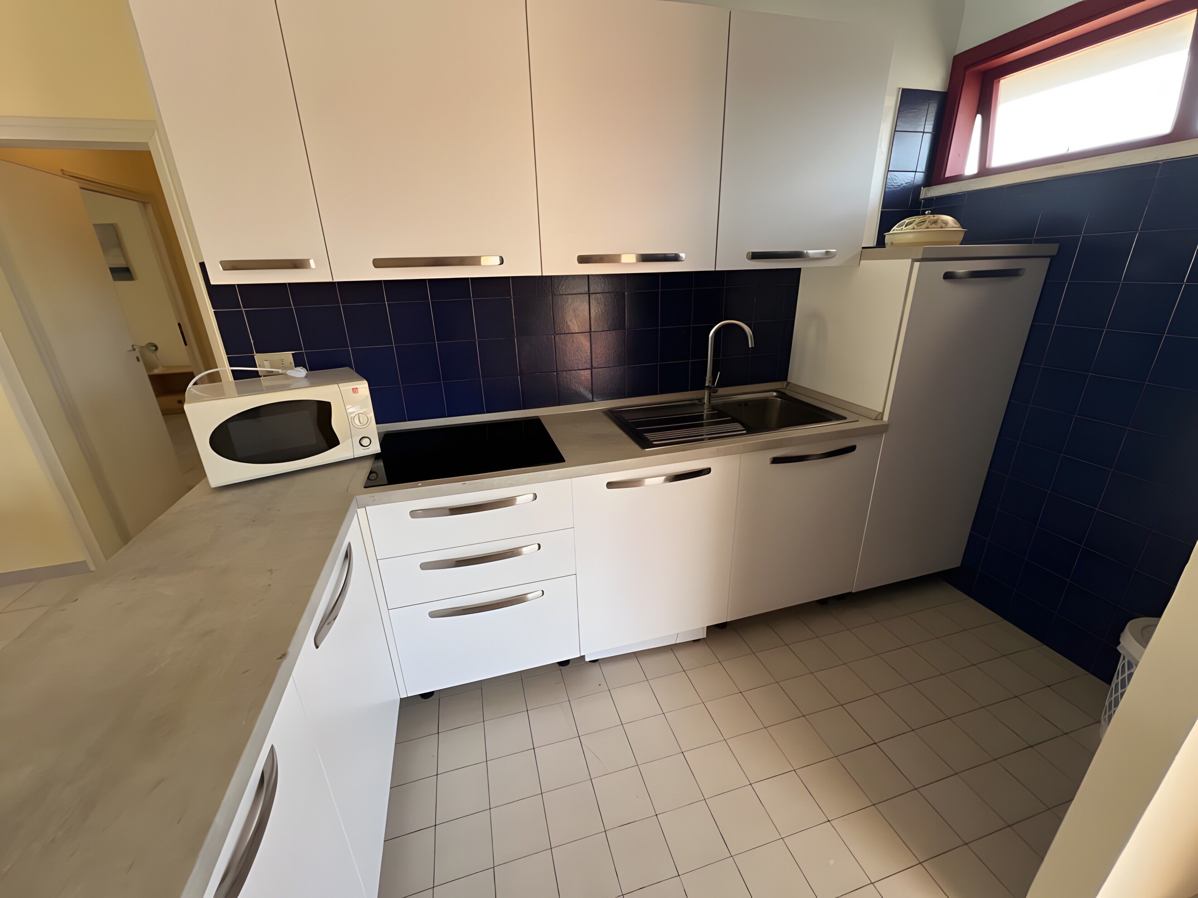 A compact kitchen with white cabinets, a microwave, a sink, and a window above the sink.