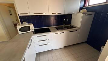 A compact kitchen with white cabinets, a microwave, a sink, and a window above the sink.