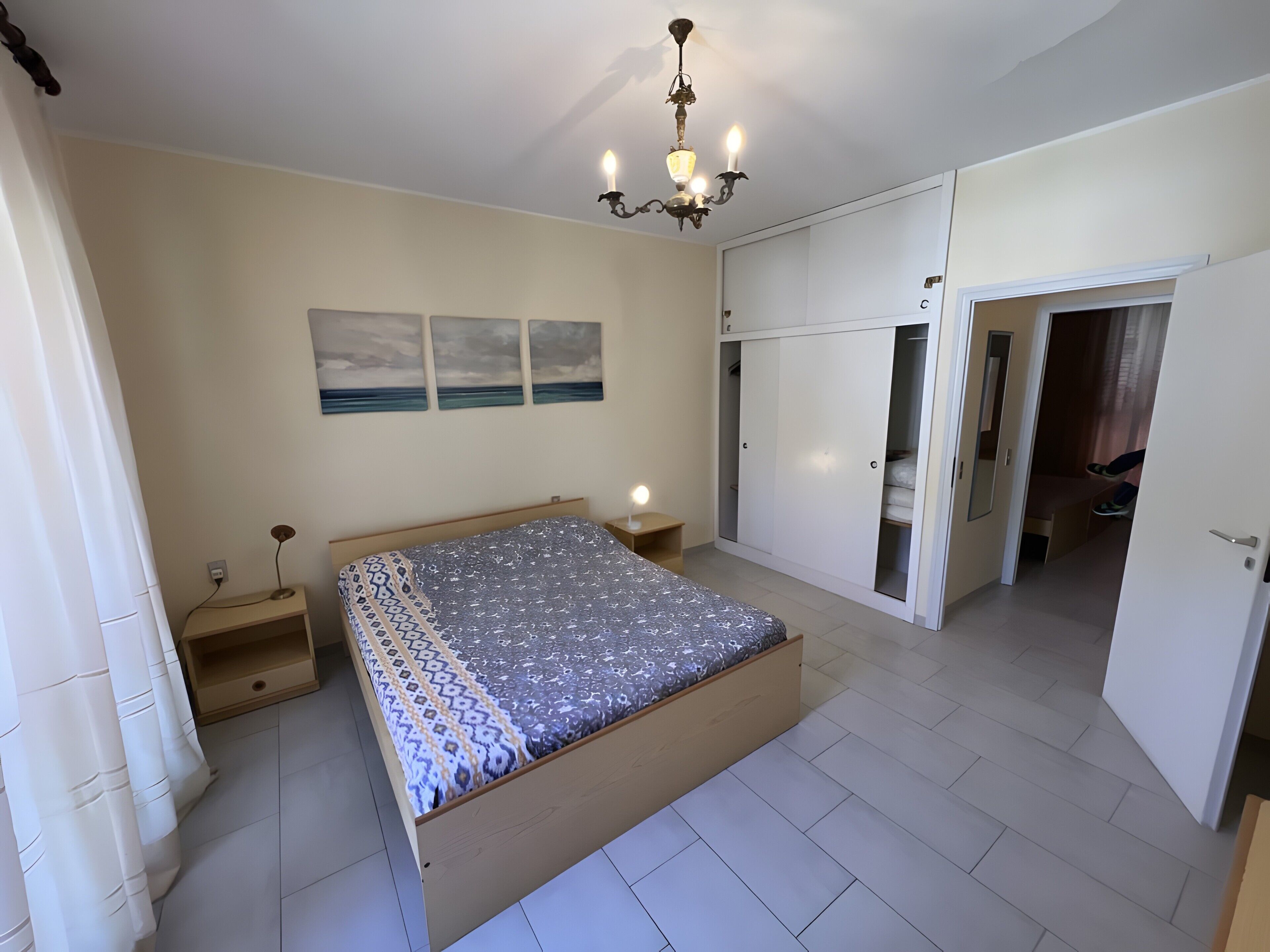 A bedroom with a bed, bedside table, lamp, wardrobe, and a ceiling light fixture.