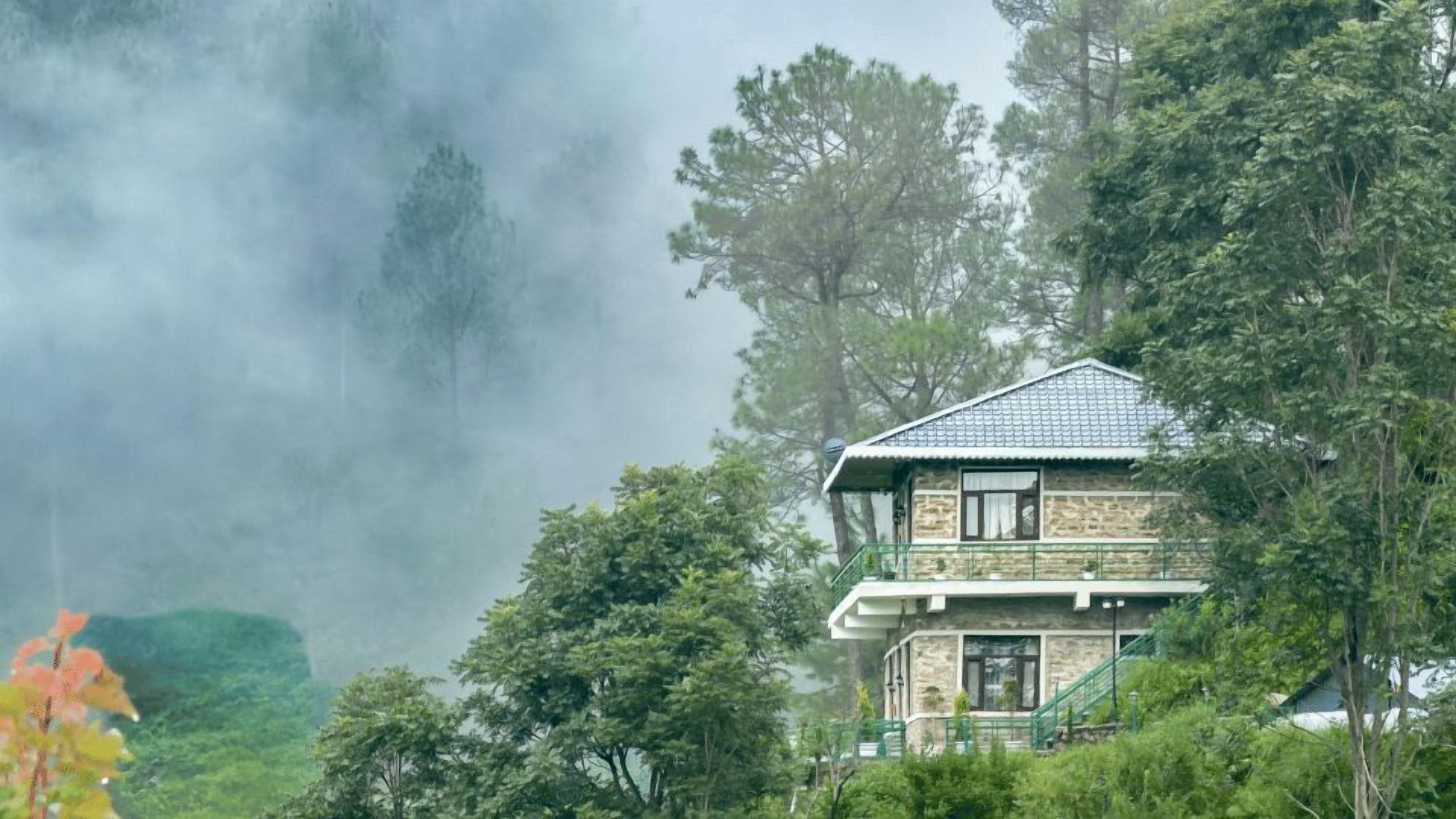 A two-story building with a stone facade and a tiled roof, surrounded by dense trees and fog.
