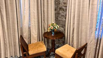 Ein Zimmer mit zwei Holzstühlen, einem runden Holztisch mit einer Blumenvase und Vorhängen.