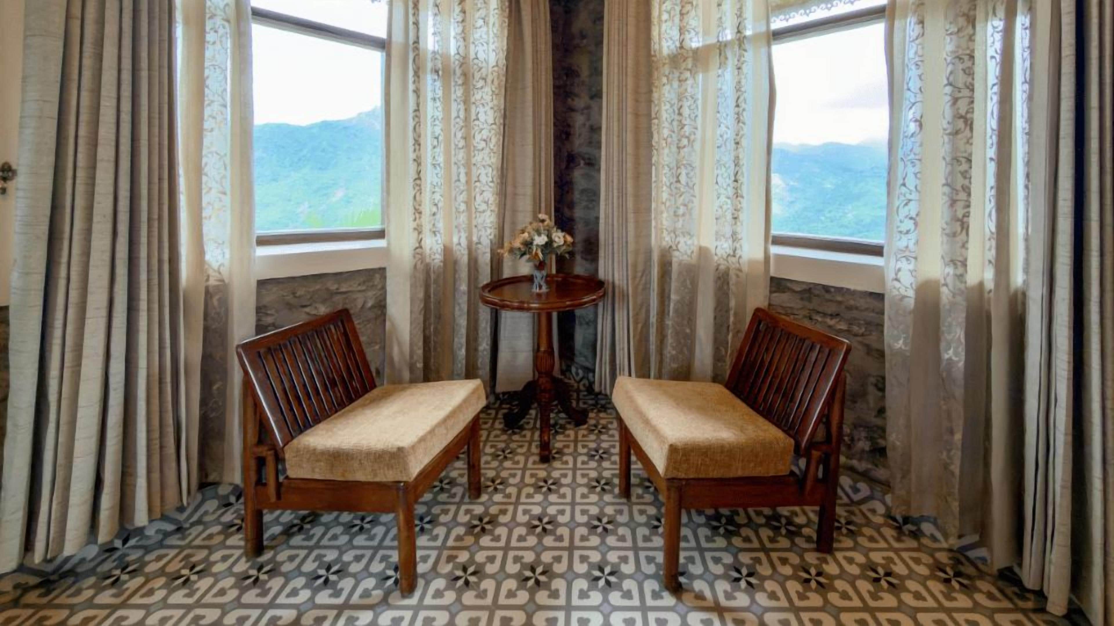 Ein Zimmer mit zwei Holzstühlen mit gepolsterten Sitzen, einem kleinen runden Tisch mit Blumenvase und einem gemusterten Boden.
