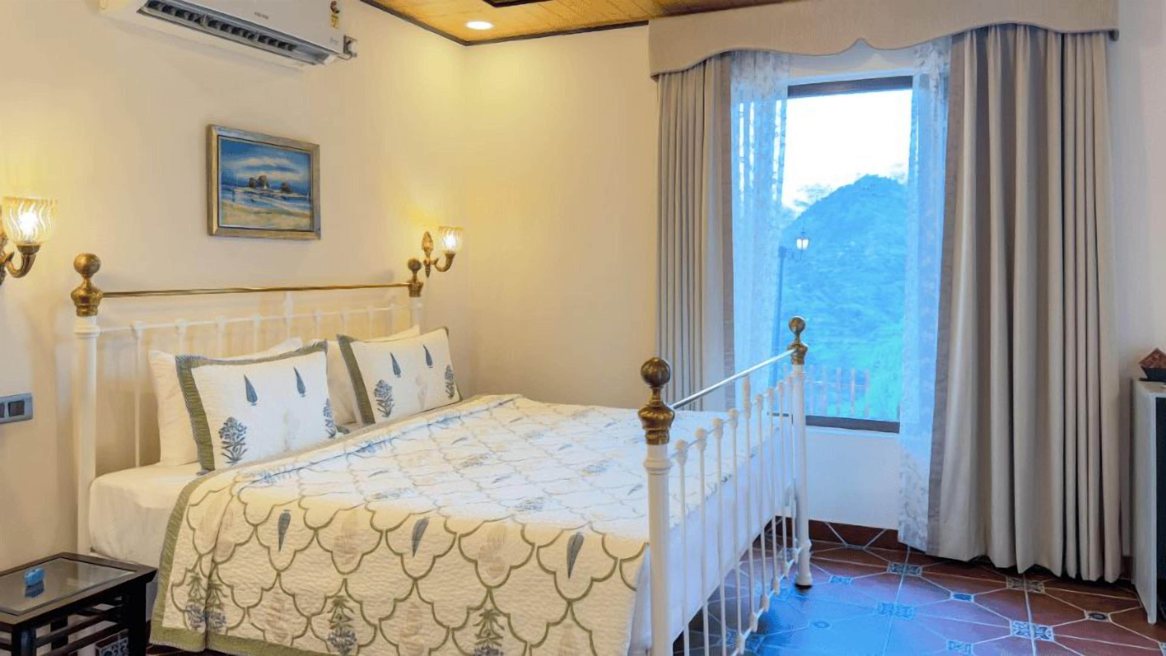 A bedroom with a bed, a nightstand, a lamp, a painting, and a window with curtains.