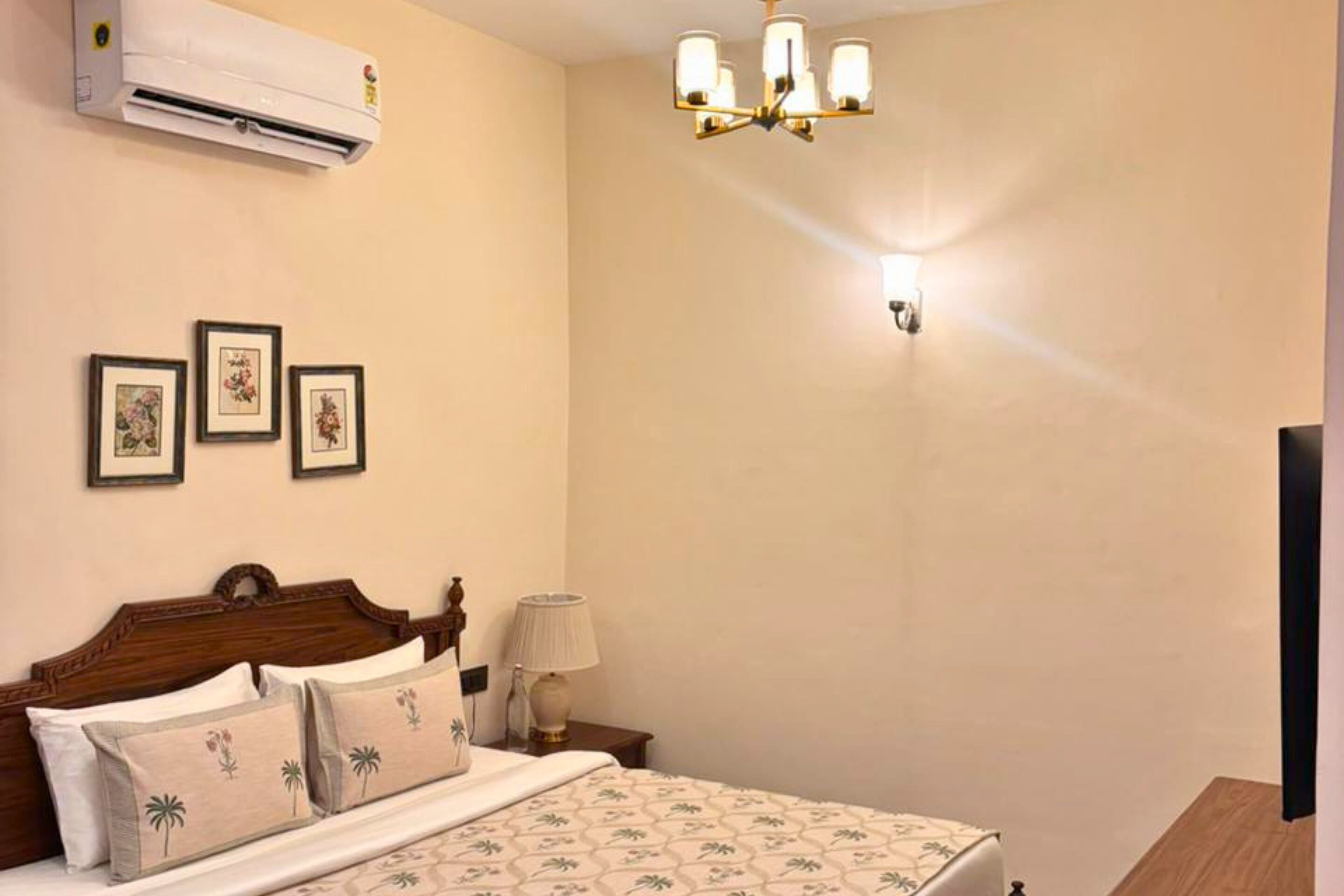 Hotelkamer met een bed, een wandairconditioner, ingekaderde foto's, een kroonluchter en een bedlampje.