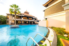 Uma piscina com uma palmeira, um edifício com varandas e céu claro.
