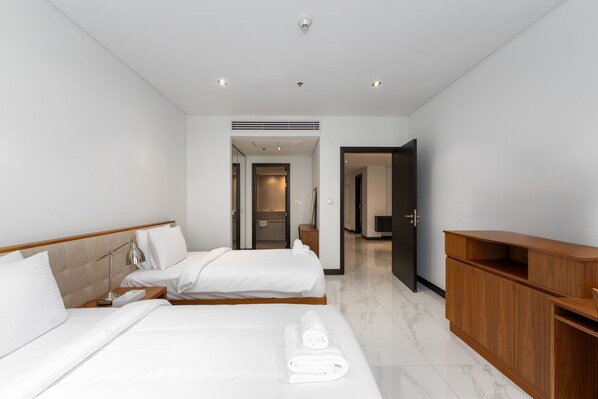 Quarto de hotel moderno com uma cama grande, uma mesa de cabeceira de madeira, uma escrivaninha e um guarda-roupa.