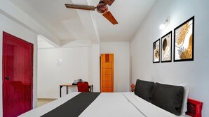 A hotel room with a bed, a desk, a chair, a red door, an orange door, and ceiling fans. - Deluxe Olive Residency (Kottayam)