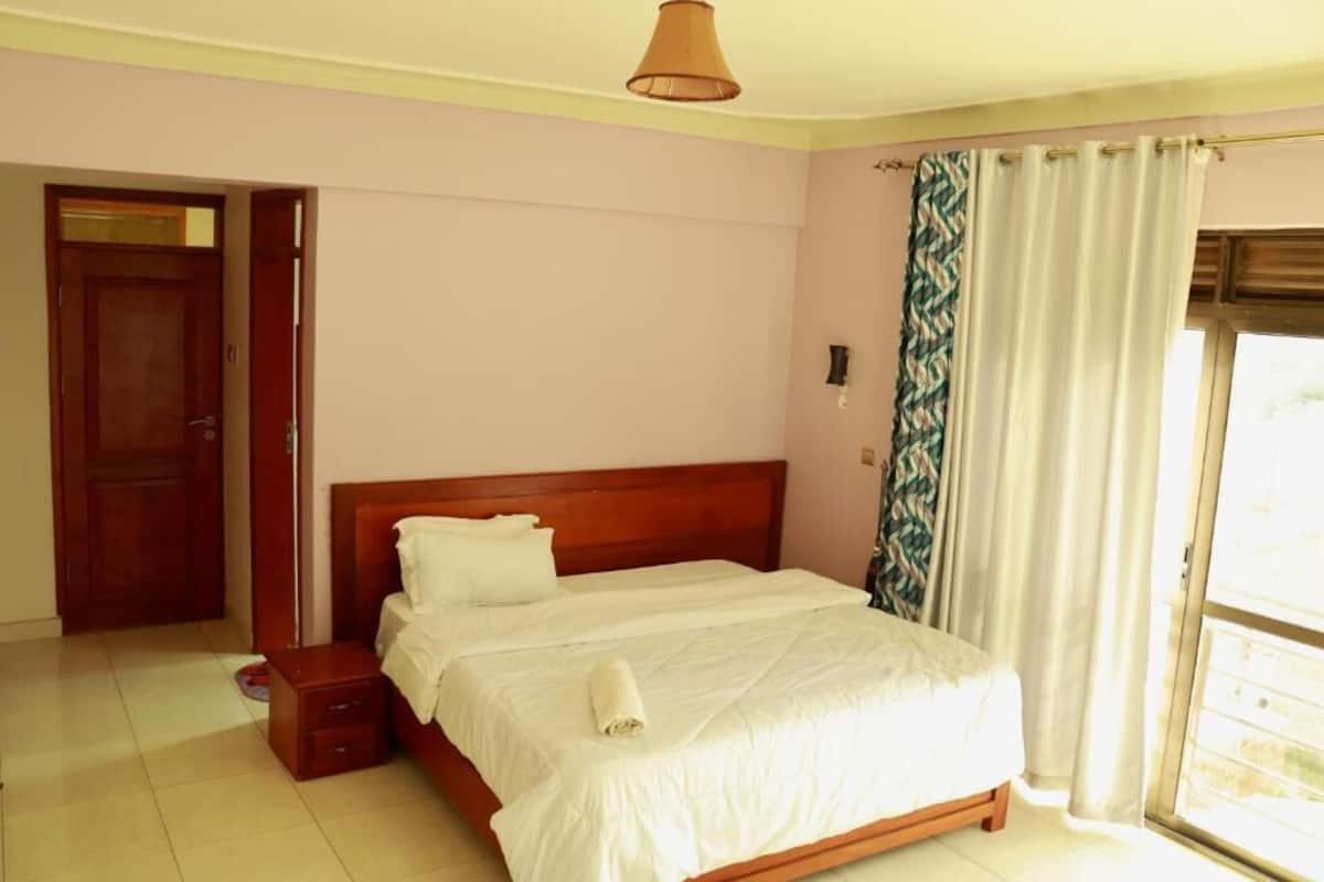 Un dormitorio con cama de madera, mesita de noche, una puerta y una ventana con cortinas.