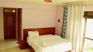 A bedroom with a wooden bed, a nightstand, a door, and a window with curtains.