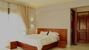 A bedroom with a wooden bed, bedside tables, a nightstand, a window with curtains, and a door.
