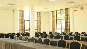 A conference room with rows of tables and chairs, large windows with curtains, and a tiled ceiling.