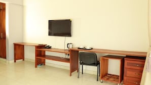 A room with a wooden desk, a black chair, a television mounted on the wall, and a small cabinet.