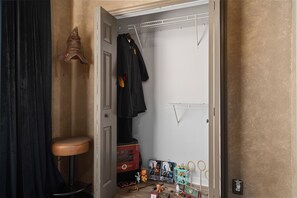 Een kast met een kledingroede, een krukje, en verschillende spullen zoals een speeltrein, een pluche knuffel en verpakte artikelen.