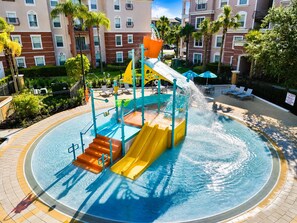 Ein Wasserpark mit Rutschen und Schwimmbecken, umgeben von einem Gebäude mit Balkonen und Palmen.