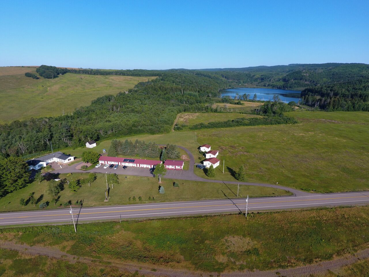 Une vue aérienne d’une zone rurale, avec une route, un grand bâtiment doté d’un toit rouge et un lac en arrière-plan.