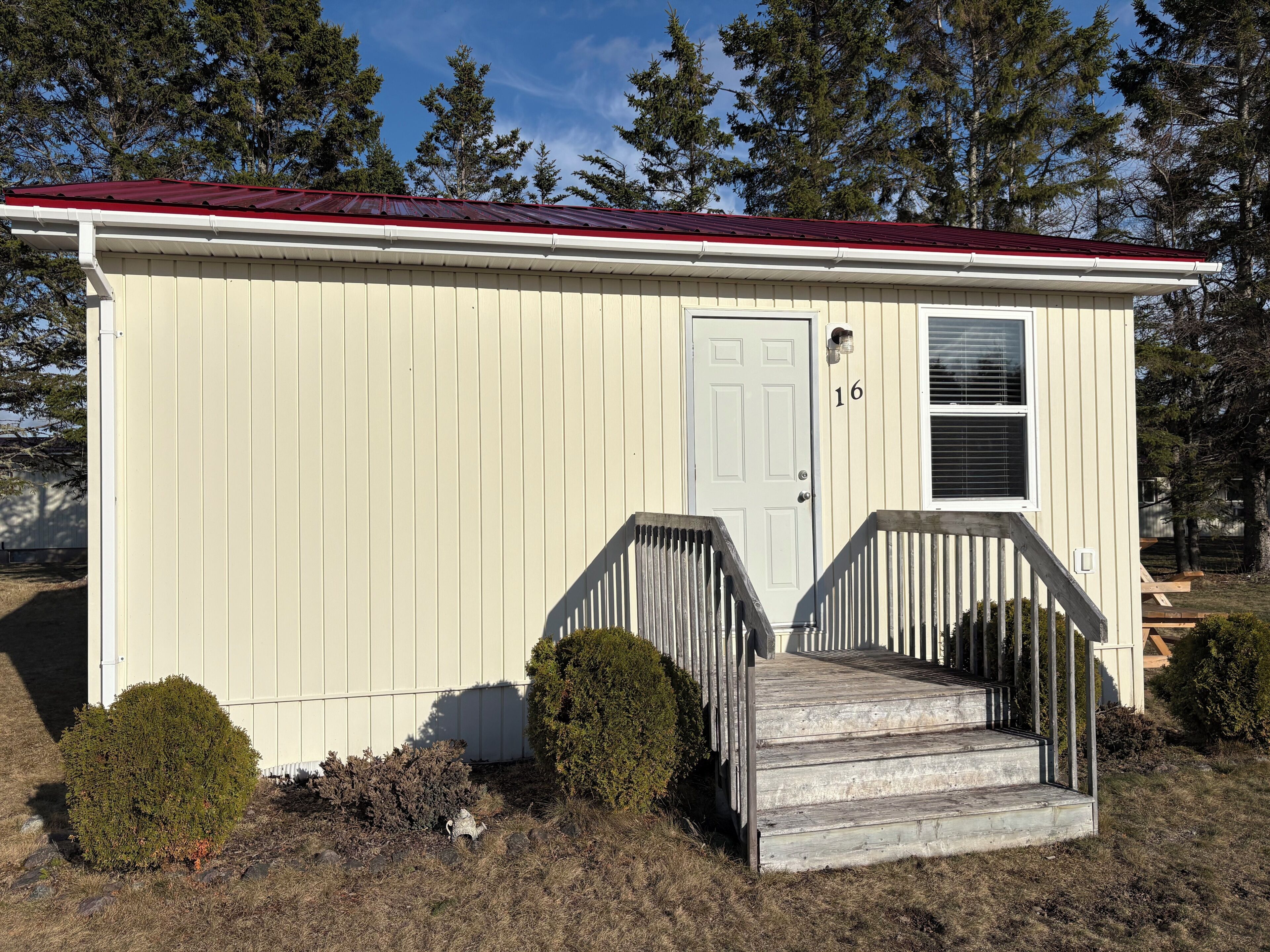 A small, single-story building with a red roof, a white door, and a small porch with steps.