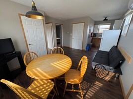 A dining area with a round table and chairs, a black TV stand, and a black sofa in a living area.