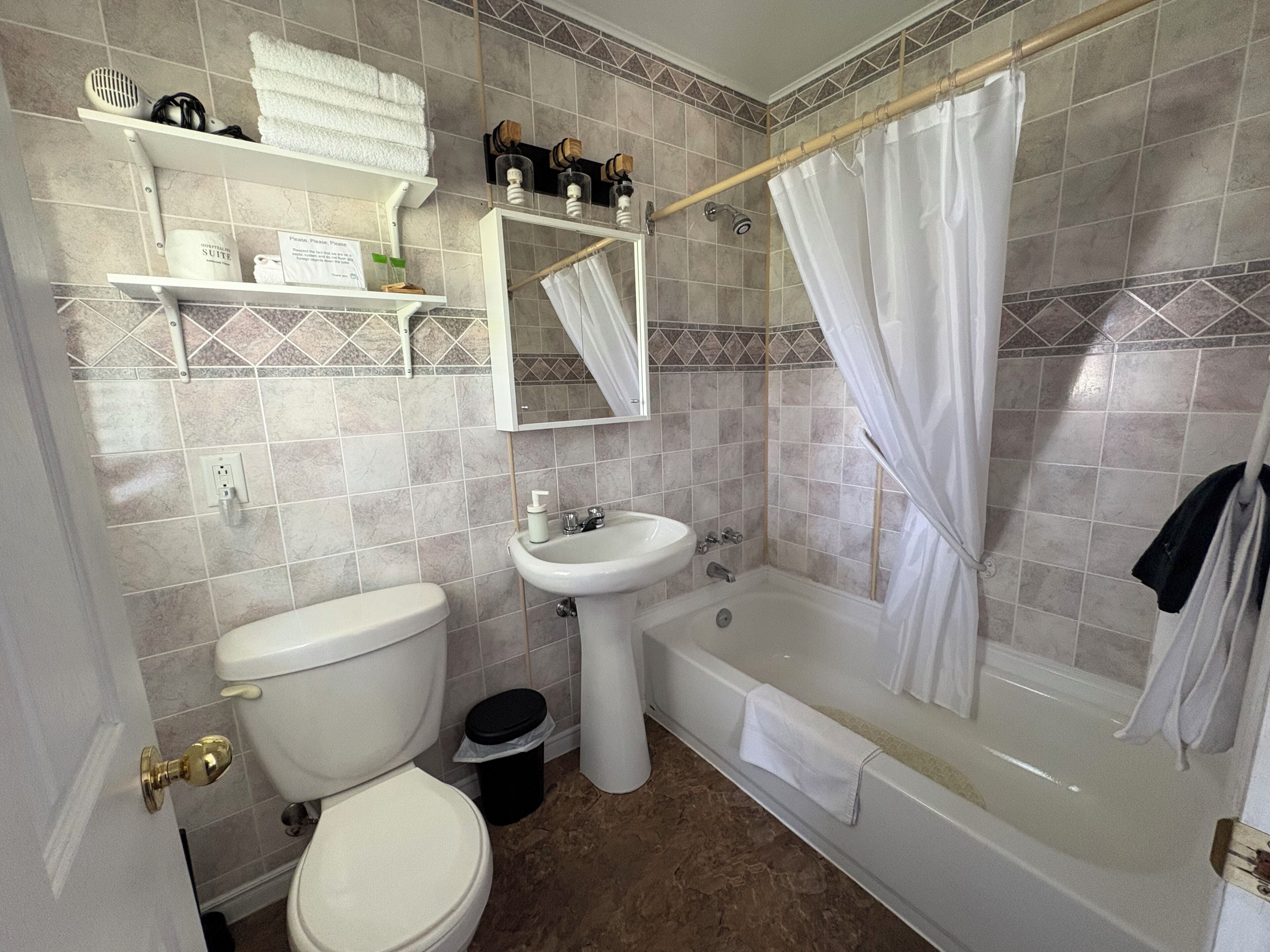 A bathroom with a toilet, sink, bathtub, shower curtain, and a towel rack.