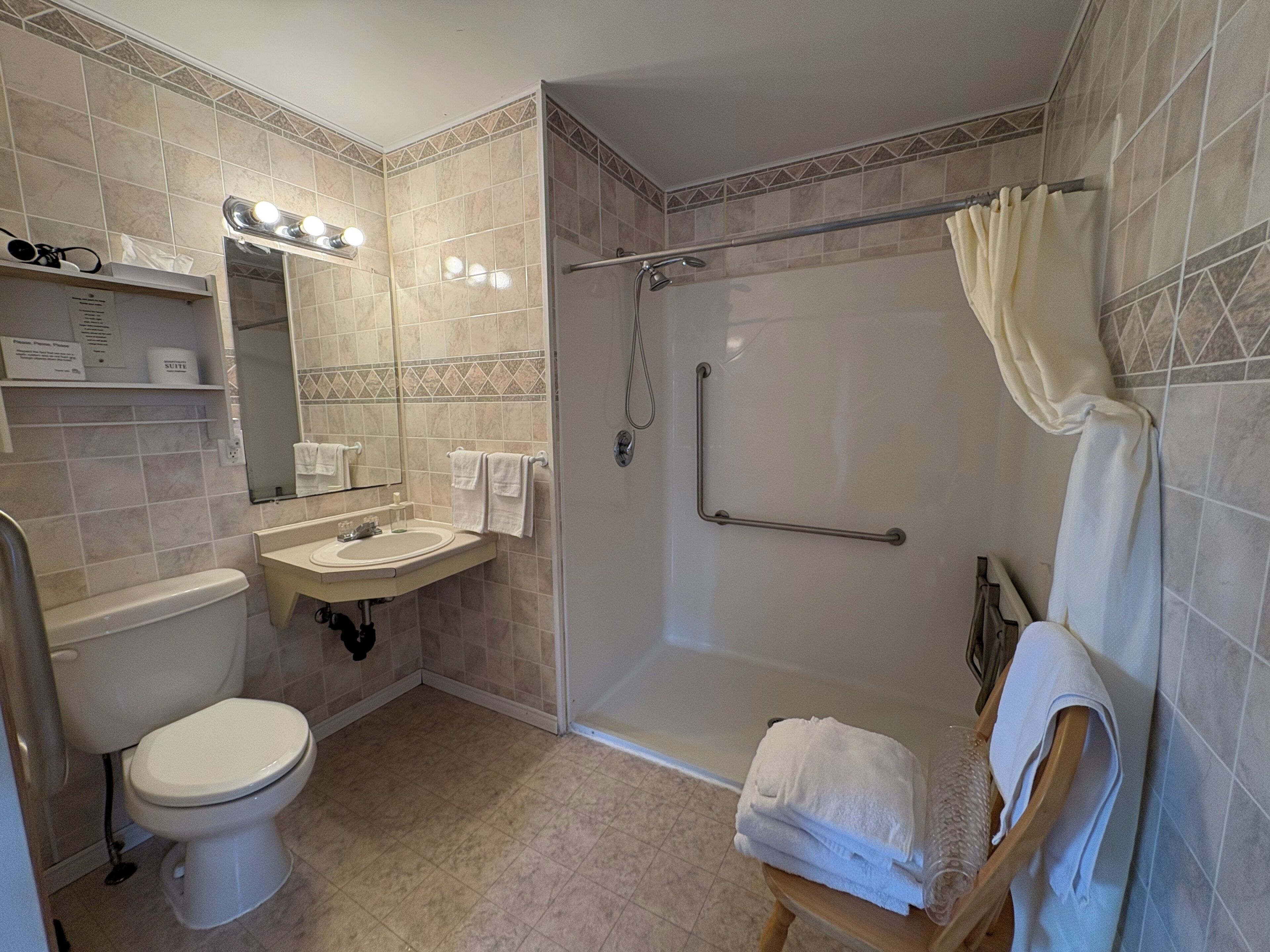 A bathroom with a toilet, sink, mirror, shower, and towel rack.