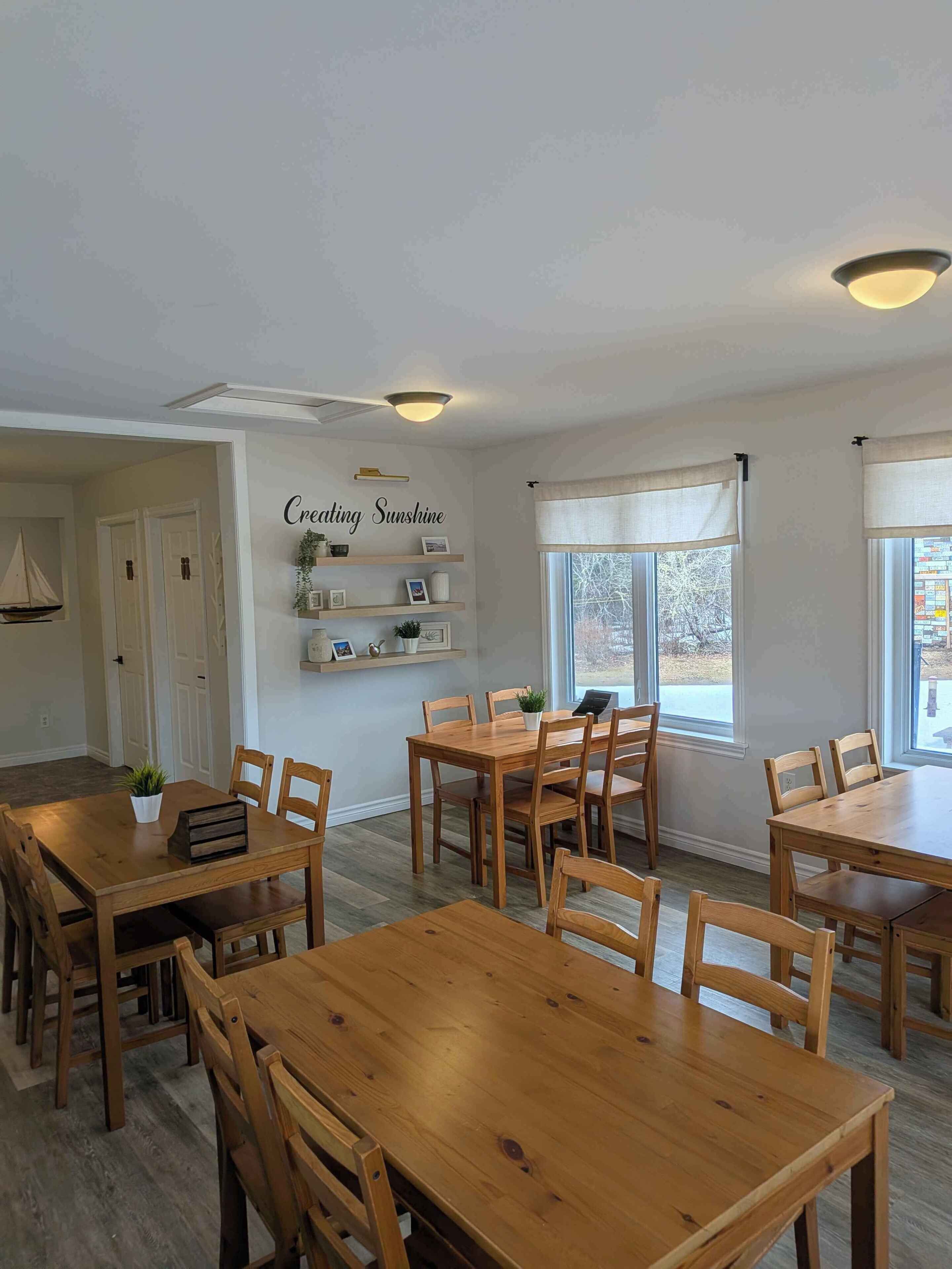 A dining area with wooden tables and chairs, a wall-mounted shelf with decorative items, and a ceiling light fixture.