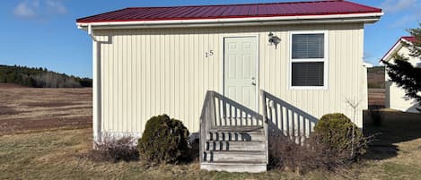 A small, single-story building with a red roof, a front door, and a staircase leading to the entrance.