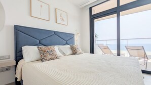 Ein modernes Schlafzimmer mit einem großen Bett, Blick auf den Balkon und zwei gerahmten Kunstwerken an der Wand.